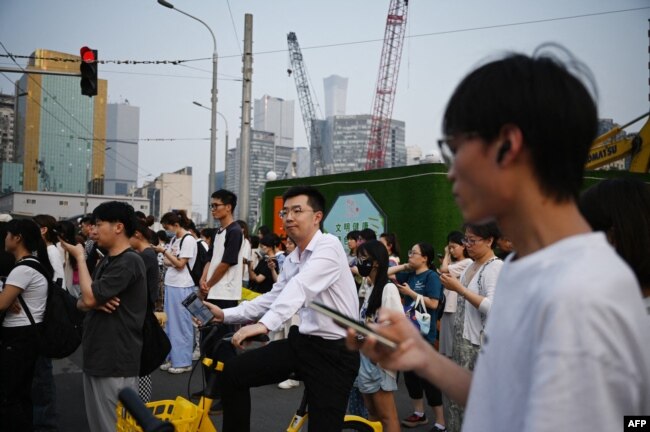 FILE - People wait to cross a road near a construction site in Beijing on July 9, 2024. China said on September 13 it would gradually raise its statutory retirement age, as the country grapples with a looming demographic crisis and an older population. (Photo by Greg Baker / AFP)