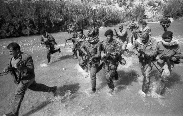 Uniformed armed men running through water